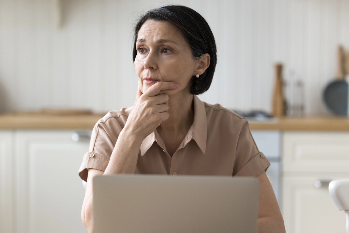 brooding woman deep in thought sit at table with laptop