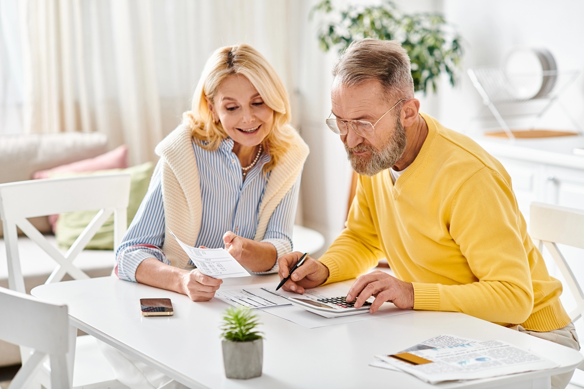 a mature couple sitting together at a table using a calculator and doing finances together