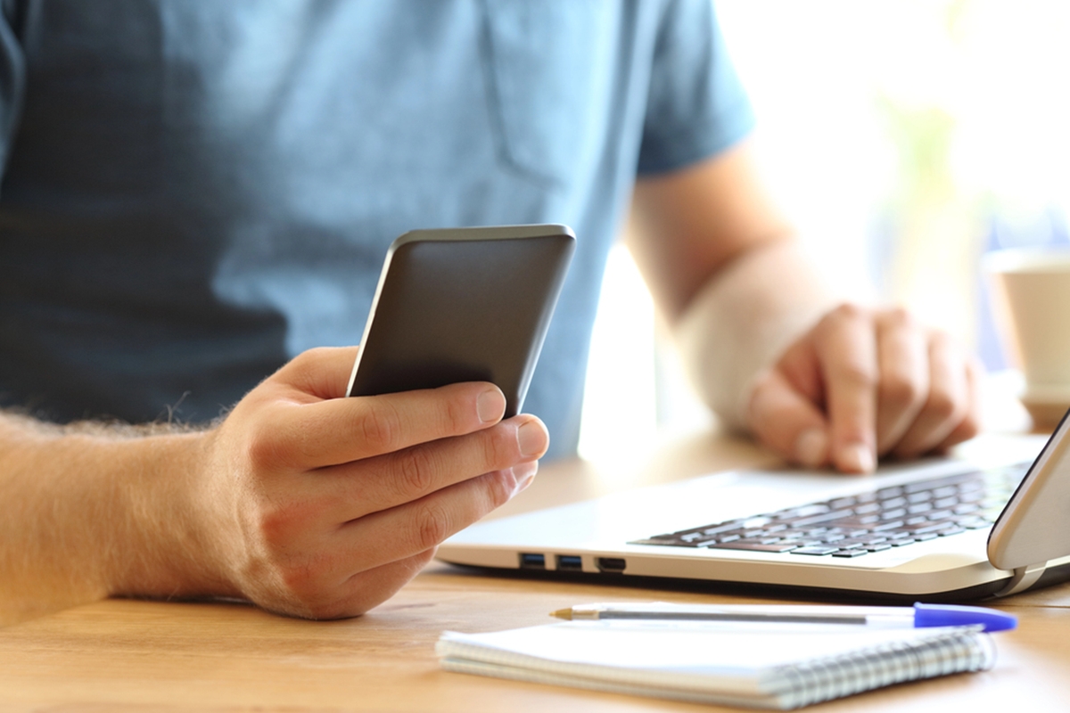 man's hands using a smartphone on a laptop