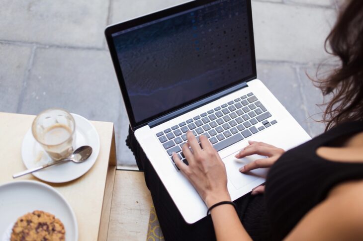woman types on her laptop while seated on a bench, engaged in her work in a public space